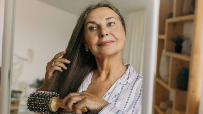 Una mujer mayor cepillando su largo cabello castaño en el espejo