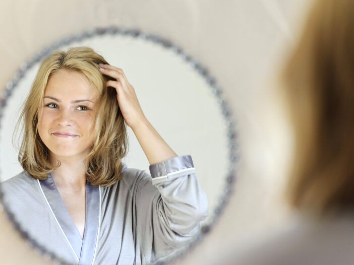 Mujer tocándose el pelo en el espejo.