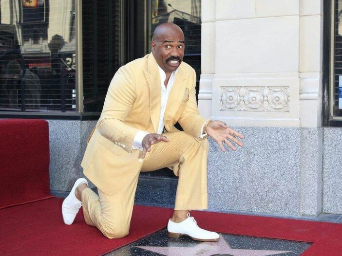 Steve Harvey sonríe con un traje amarillo mientras se arrodilla frente a su estrella de Hollywood Blvd.