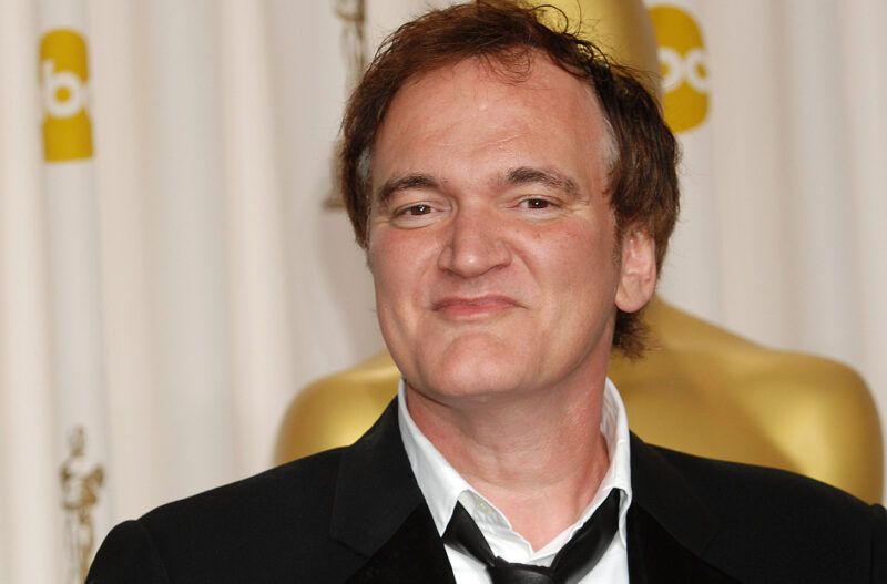 Quentinas Tarantino įžūliai šypsosi su kostiumu.