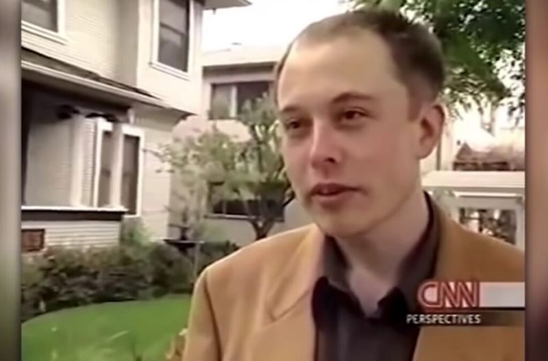 Elon Musk poartă o jachetă maro.