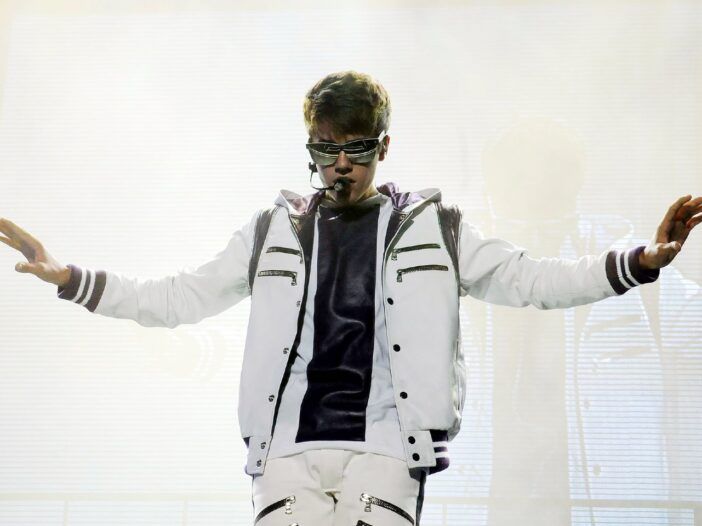 Justin Bieber i en vit jacka håller händerna ut åt sidan.