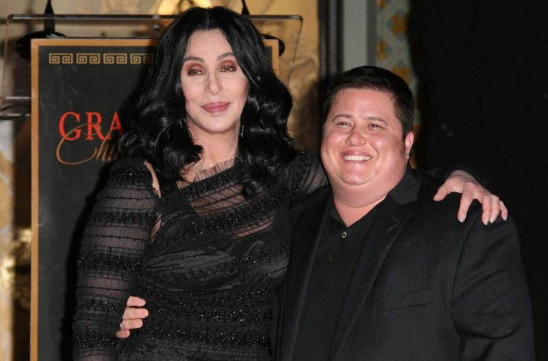 Cher on mustas kleidis ja naeratab, käsi ümber oma poja Chaz Bono, kes kannab musta ülikonda.