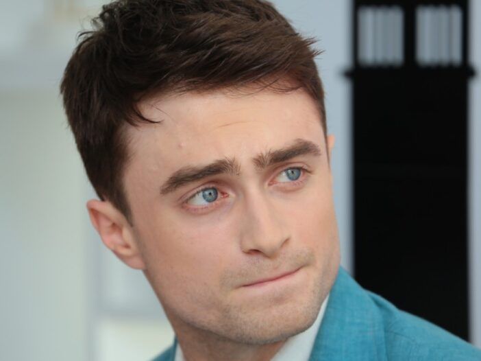 Daniel Radcliffe sa pozerá nabok a má na sebe modrý oblek, ktorý ladí s jeho zasnenými očami