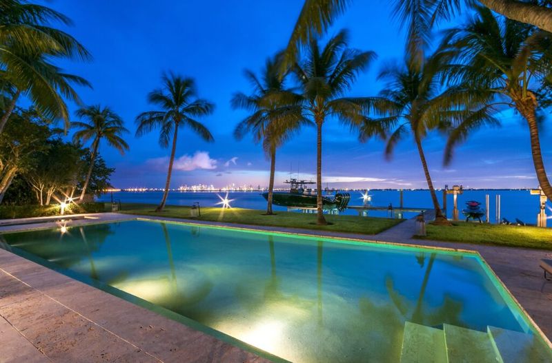 una foto de una piscina al aire libre frente al agua con palmeras