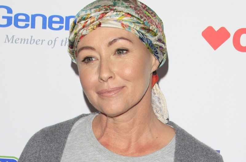 Shannen Doherty sonriendo en un evento de lucha contra el cáncer con un colorido pañuelo en la cabeza.