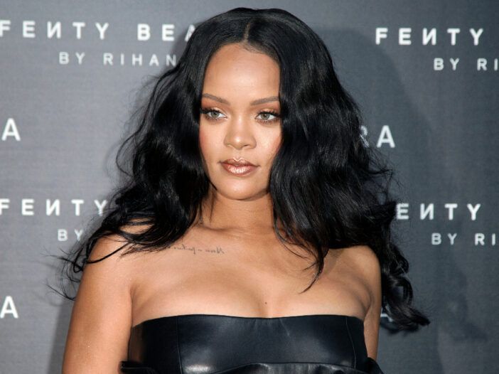 Rihanna poartă o rochie neagră în fața unui fundal gri