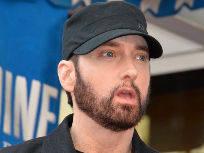 Eminem usa una chaqueta oscura y un sombrero mientras da un discurso.