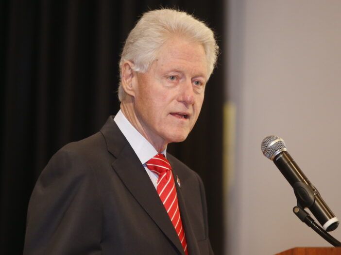 Bill Clinton într-o jachetă neagră și cravată roșie vorbind la microfon