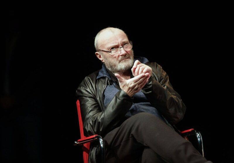 Phil Collins hablando en el escenario en una silla