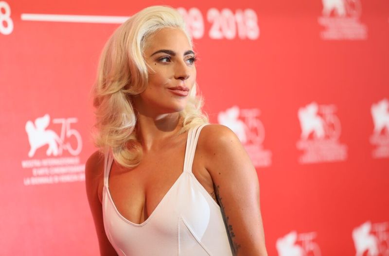 Lady Gaga har på seg en hvit kjole mens hun står mot en rød bakgrunn