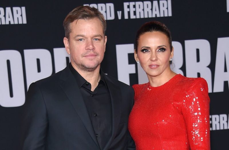 Matt Damon con un traje negro de pie con su esposa Luciana con un vestido rojo