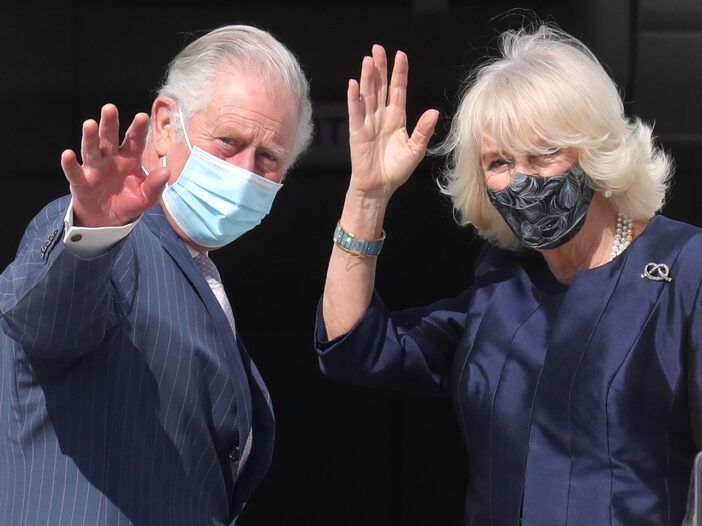 El príncipe Carlos a la izquierda, Camilla Parker Bowles a la derecha, saludando y con máscaras.