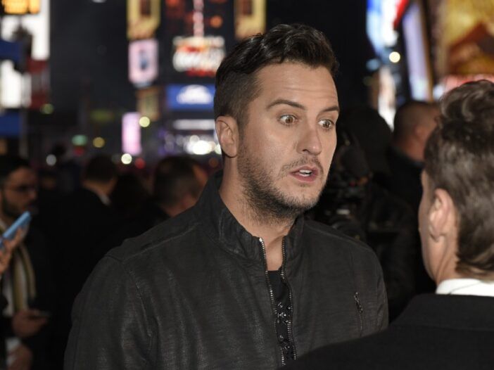 Luke Bryan, vestido con una chaqueta negra, habla con un hombre en Times Square