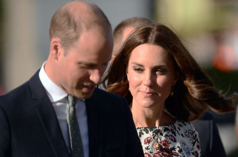 Tamsų kostiumą ir žalią kaklaraištį vilkintis princas Williamas vaikšto su Kate Middleton, vilkėdamas gėlėta suknele