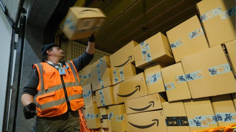 Un lucrător Amazon încarcă o cutie într-un camion în timp ce poartă o haină de siguranță portocalie