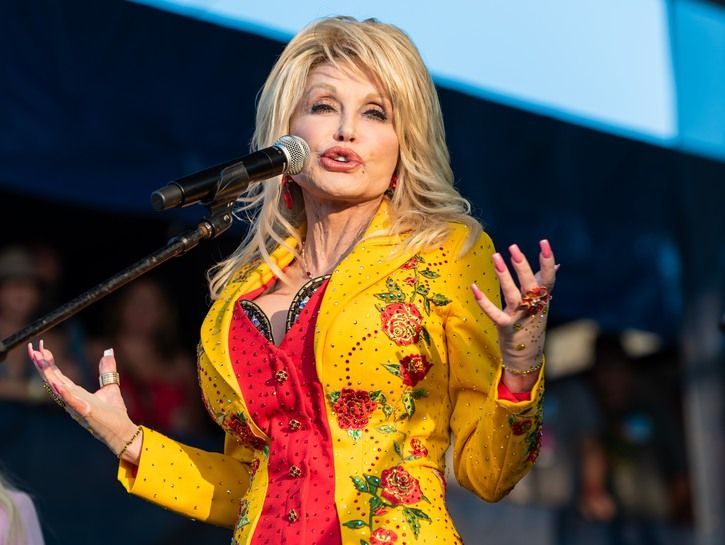 Dolly Parton scenoje dėvi ryškiai raudoną ir geltoną aprangą, kai kreipiasi į publiką