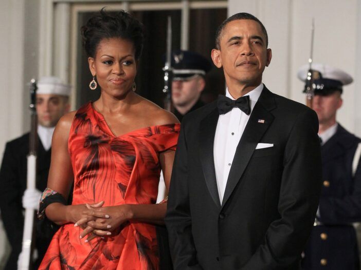 Michelle Obama v červených šatách s kvetinovou potlačou stojí pred Bielym domom s Barackom v smokingu