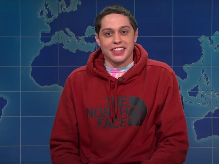 captura de pantalla de Pete Davidson en Weekend Update en SNL con una sudadera con capucha roja puesta