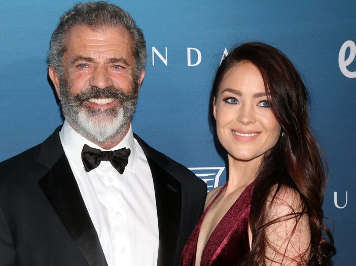 Mel Gibson Usmievajúci sa v smokingu, stojaci s Rosalind Ross v červených šatách.
