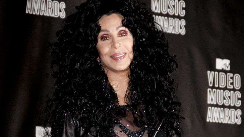 Cher má na červenom koberci veľkú čiernu parochňu, koženú bundu a trblietavý oblek