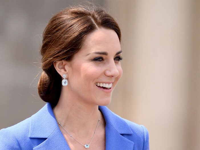 Kate Middleton šypsosi. dėvi mėlyną viršutinę dalį