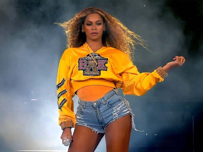 Beyonce actuando con una camiseta amarilla y pantalones cortos de mezclilla