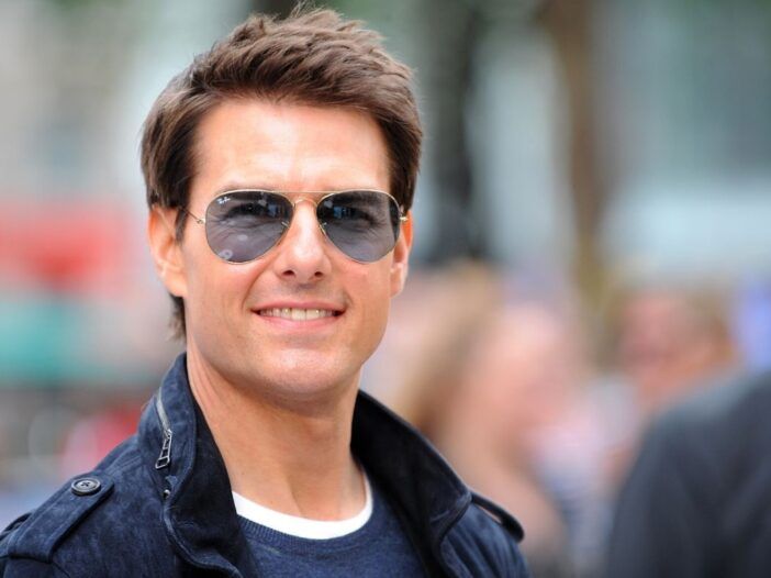 Tom Cruise con chaqueta azul, camiseta azul y gafas de sol en la alfombra roja