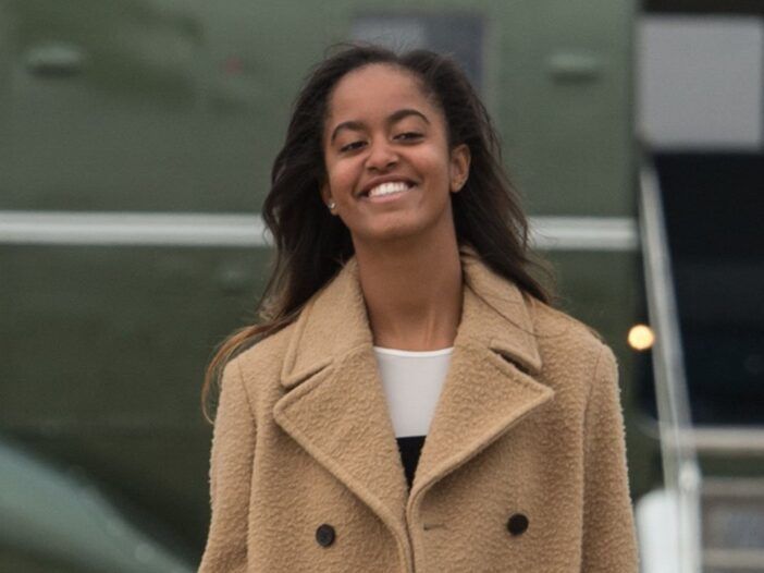 Malia Obama smiler i en beige frakk