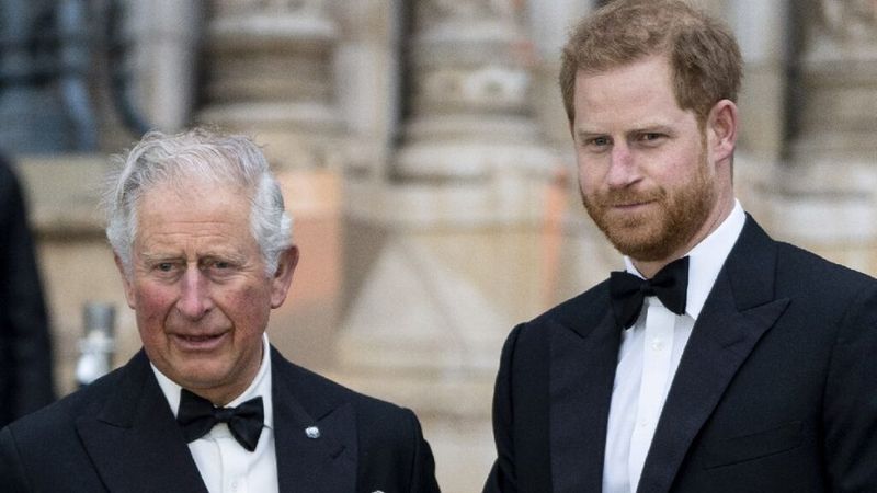 El príncipe Carlos y el príncipe Harry visten esmóquines negros mientras posan para fotos al aire libre.
