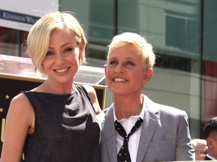 Portia de Rossi usa un vestido negro y está de pie con su esposa Ellen DeGeneres, en un traje gris.
