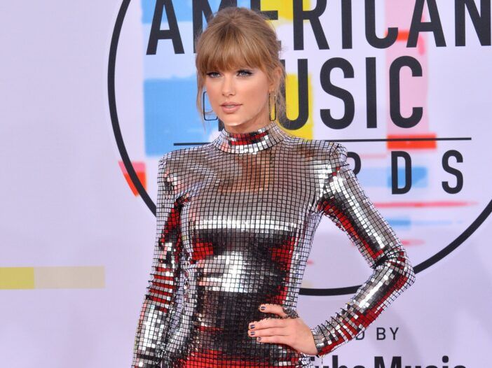 Taylor Swift con un vestido de espejo brillante, con la mano izquierda en la cadera.