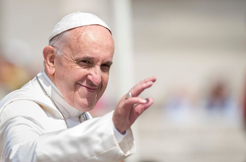 Popiežius Pranciškus šypsosi ir mojuoja.