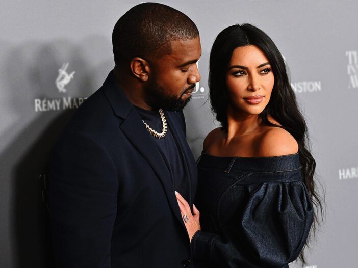Kanye West sa pozerá na Kim Kardashian, keď pózujú na sivom pozadí