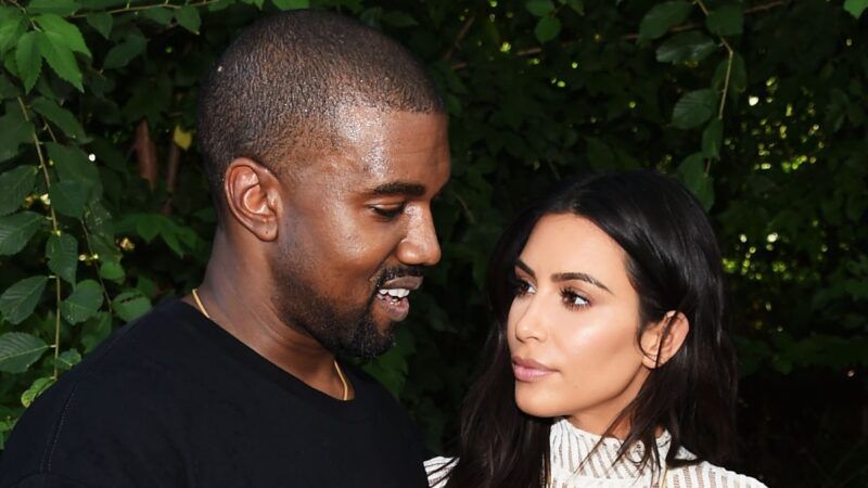 Kanye West, vestido con una camiseta negra, mira hacia abajo mientras Kim Kardashian, con un vestido de punto blanco, lo mira a él.