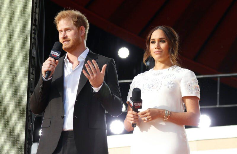 El príncipe Harry con traje negro hablando con Meghan Markle con vestido blanco