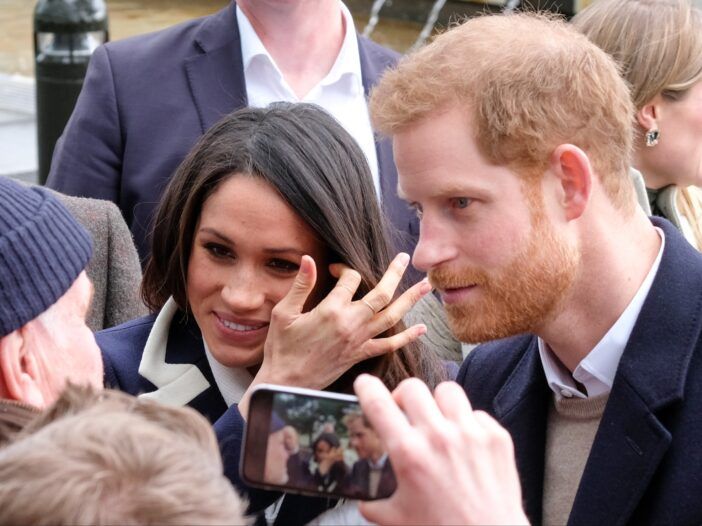 Meghan Markle smiler mens hun står sammen med prins Harry blant en mengde støttespillere