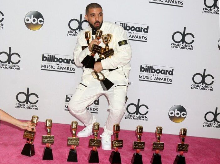 Drake vistiendo un esmoquin blanco y sosteniendo varios premios en los Billboard Music Awards