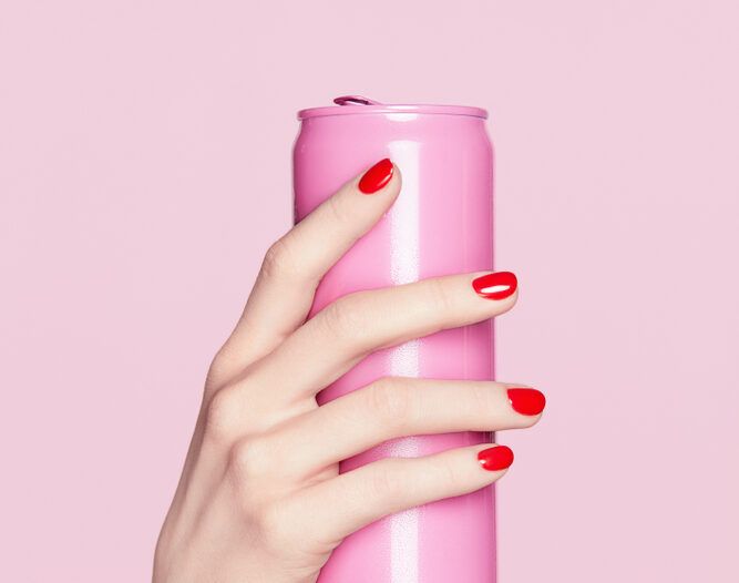 Küünte disain. Punane maniküür naise kätel. Pehme naha ja punase küünelakiga naise käsi, mis hoiab roosal taustal roosa soodapurki. Kõrgresolutsiooniga.