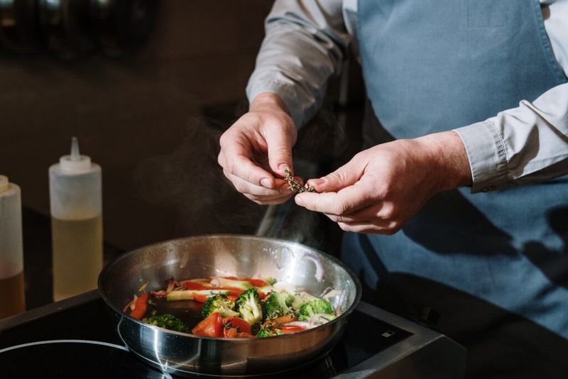 Bilde av grønnsaker som lager mat på komfyren med en mann som tilsetter krydder.