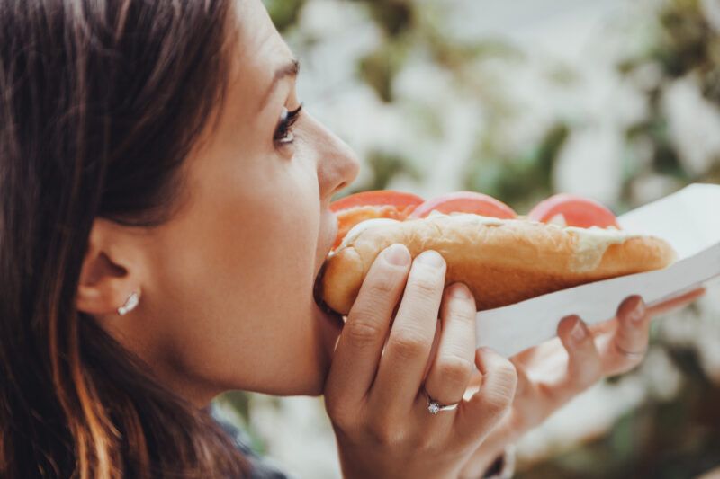 Attēls, kurā sieviete ēd hotdogu