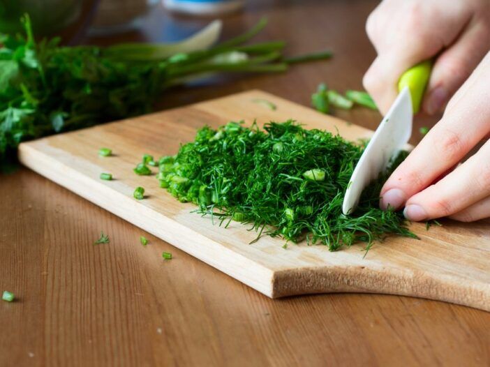 Cortar hierbas frescas con un cuchillo de cerámica sobre una tabla de madera. Cocinando