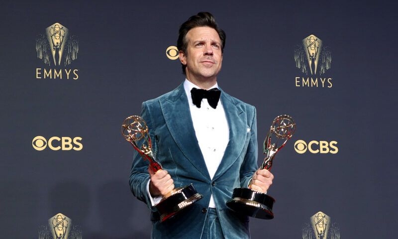 Jason Sudeikis sosteniendo dos premios Emmy con un esmoquin azul