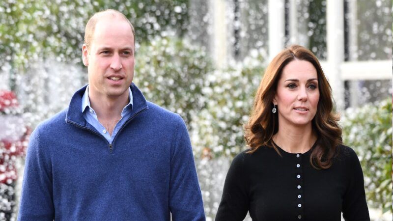 El príncipe William, con un suéter azul, camina con Kate Middleton, con un top negro, al aire libre