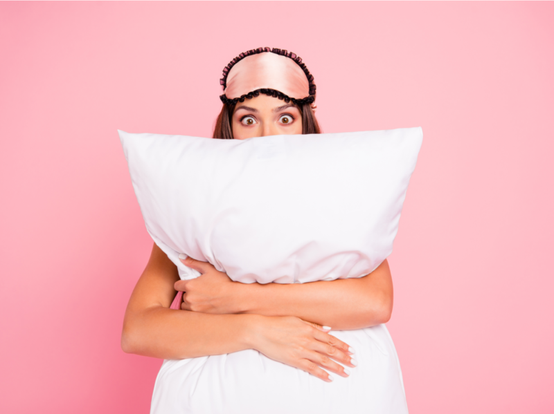mujer sorprendida con máscara para los ojos, almohada abrazadora, escondida. Aislado sobre fondo rosa pastel