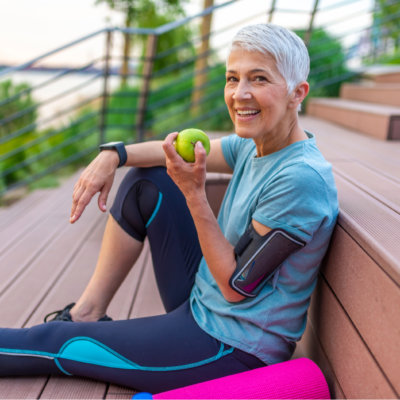 Sportiska sieviete, kas ēd ābolu. Skaista sieviete ar sirmiem matiem sešdesmito gadu sākumā, atpūšoties pēc sporta treniņiem. Veselīgs vecums. Nobriedusi, sportiska sieviete, ēdot ābolu pēc sporta treniņa