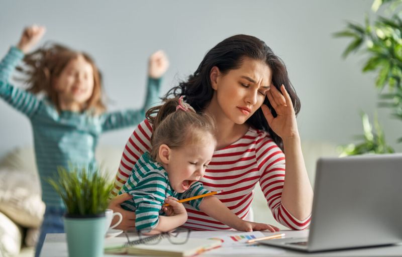 Kvinne stresset mens hun holder barn og jobber hjemmefra.