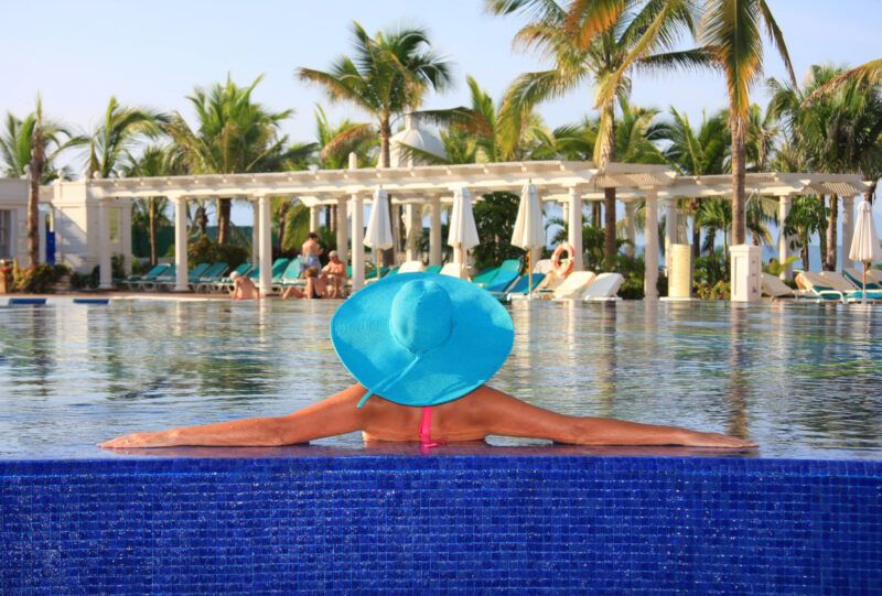 Mujer con sombrero para el sol relajándose en una piscina en un resort todo incluido.