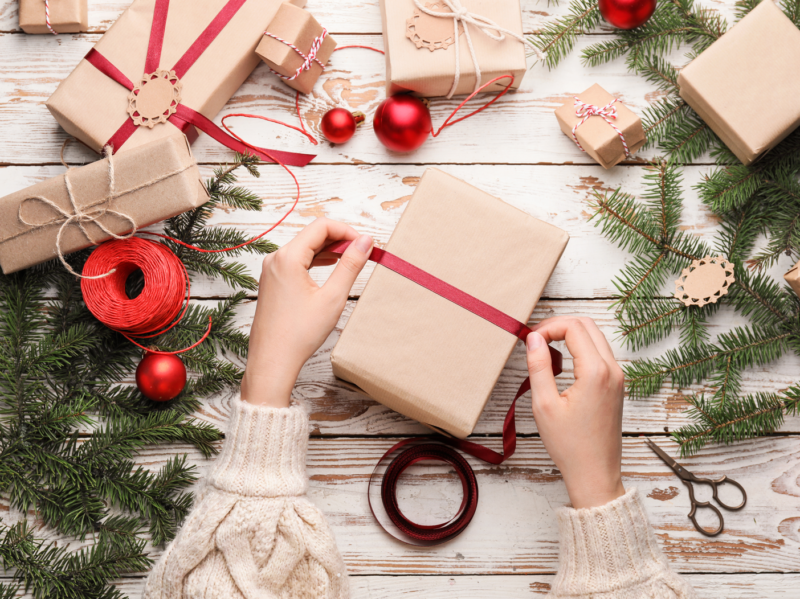 Dos manos envolviendo una cinta alrededor de un regalo, con más regalos en el fondo