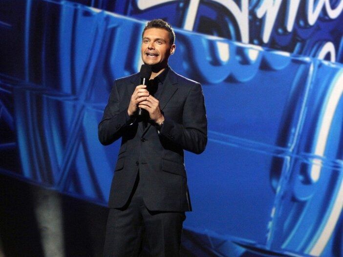 Ryan Seacrest iført mørk dress på scenen på et American Idol-arrangement